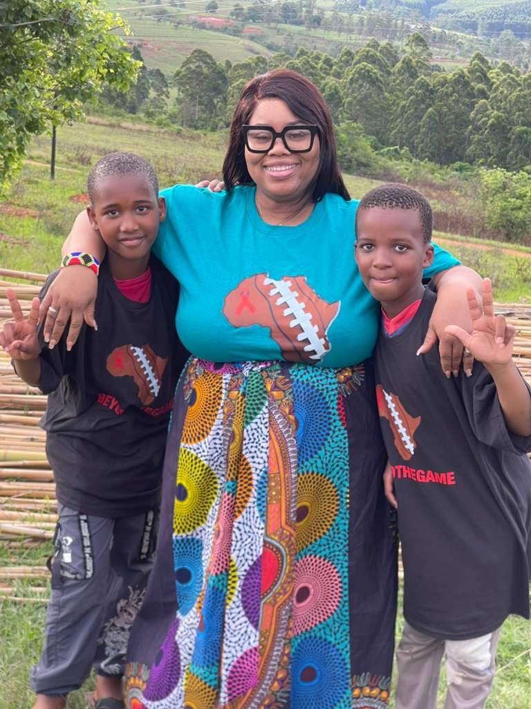A Beyond The Game volunteer with two boys in BTG shirts on a hillside in Eswatini