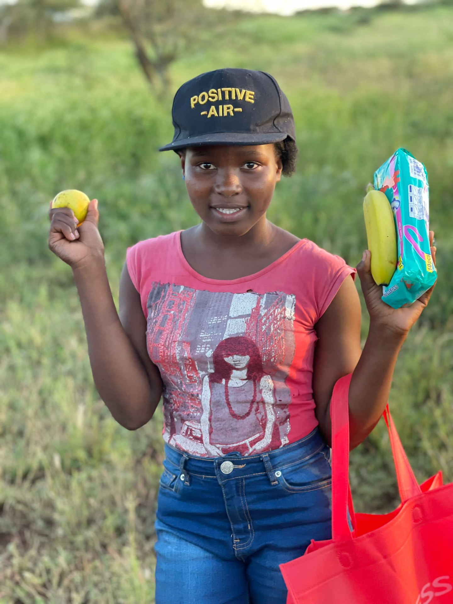 A girl holding fruit and a pack of sanitary napkins she received in Eswatini