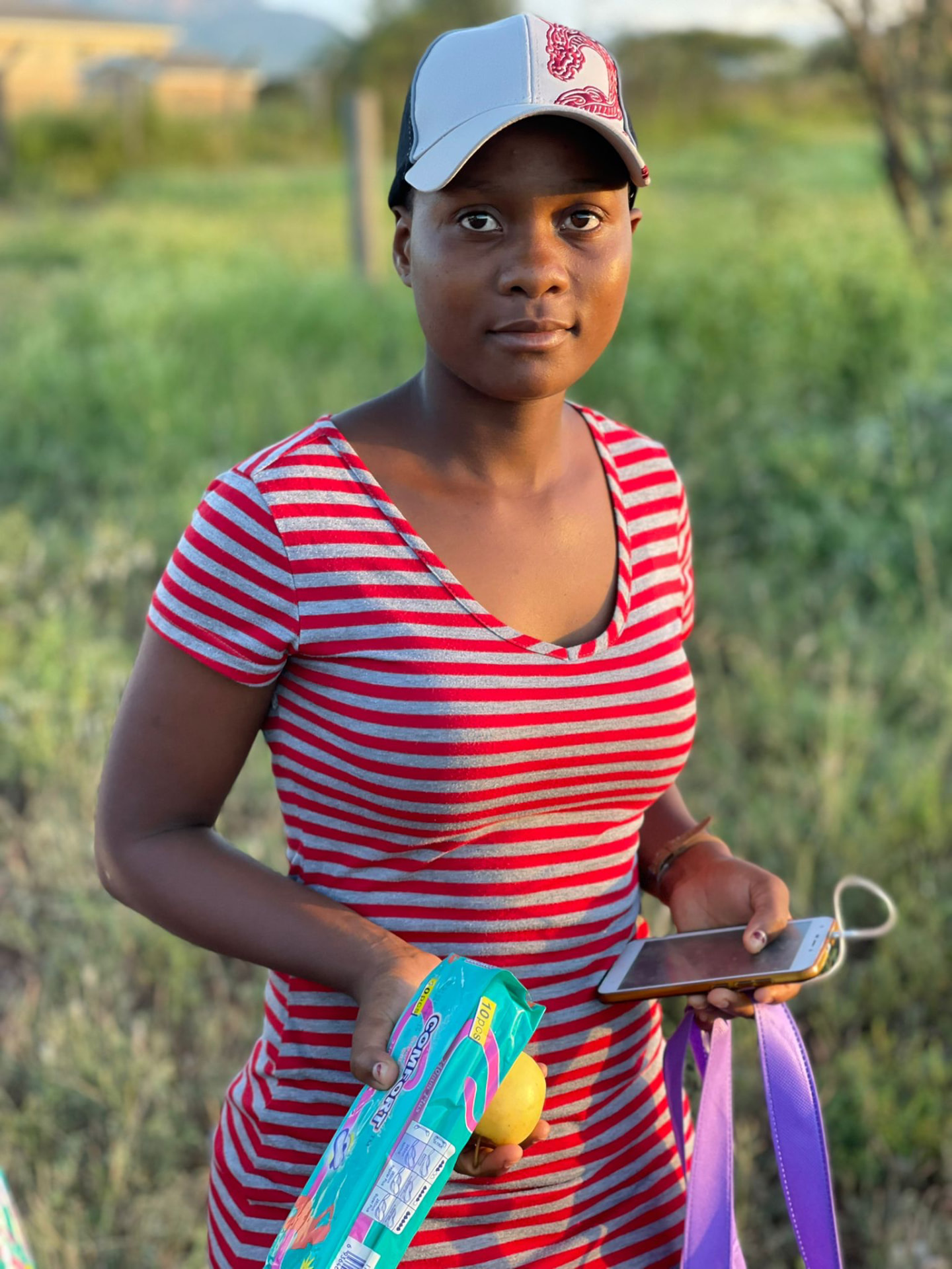 A young woman holding sanitary napkins and fruit received at a distribution