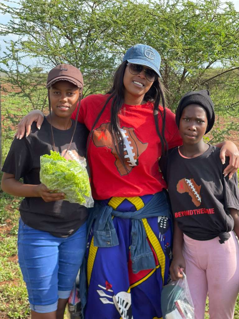 A Beyond The Game volunteer with two girls holding fresh produce from a distribution