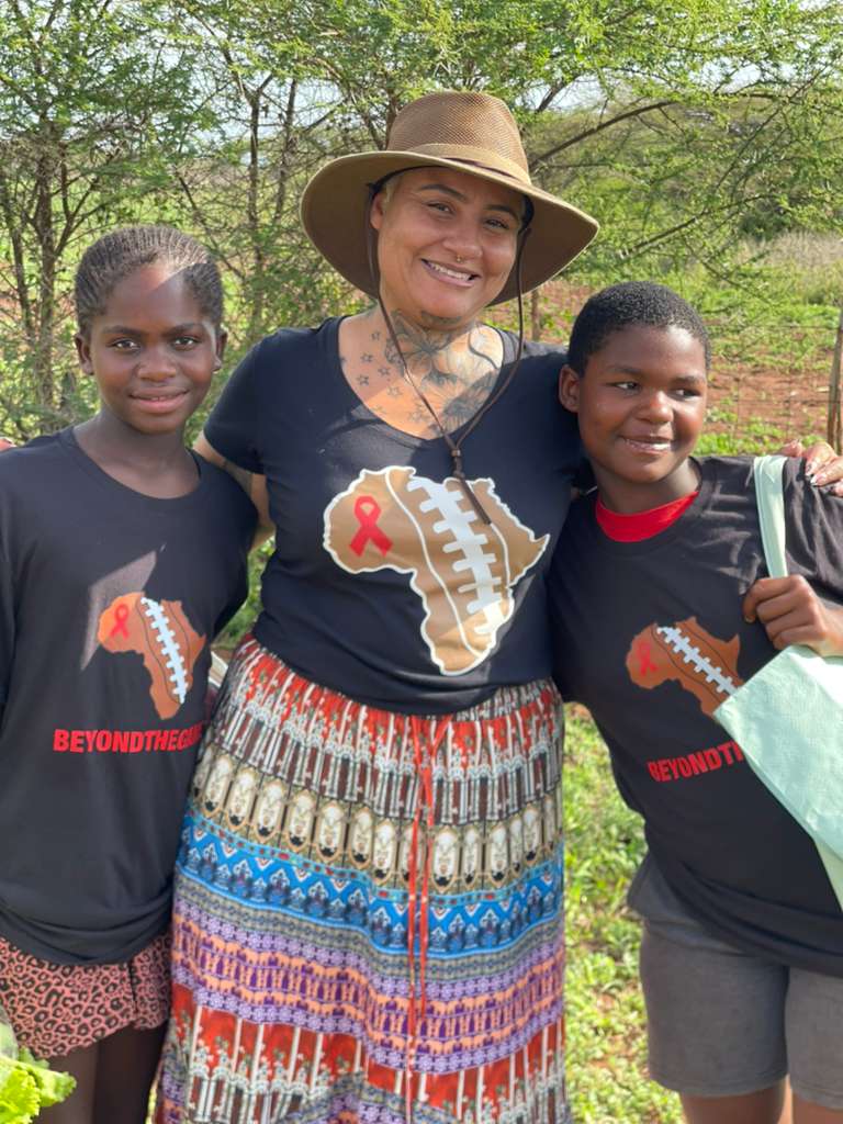 A Beyond The Game volunteer with two children carrying their food bags